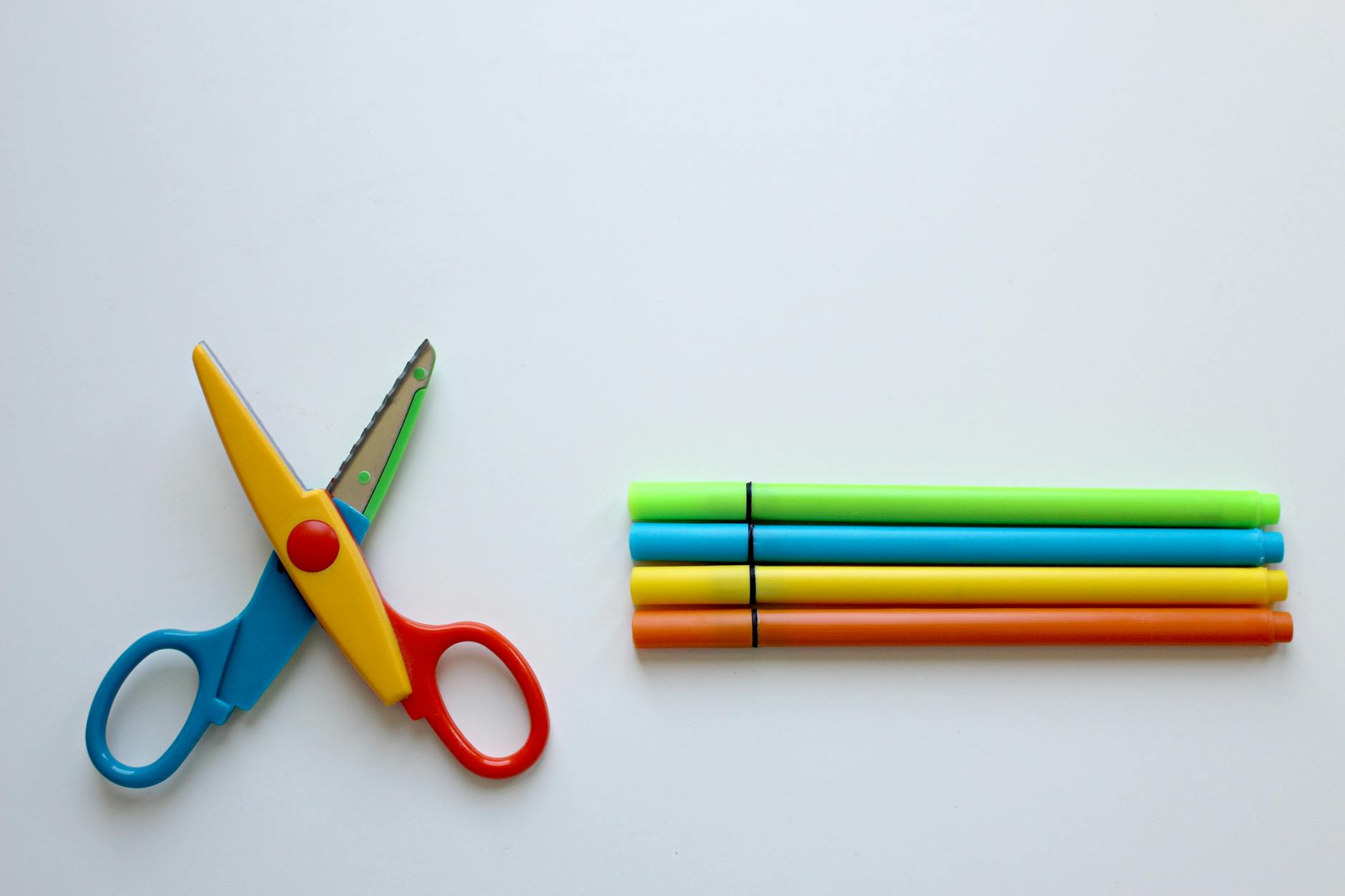 multicolored scissor and four coloring pen on white surface