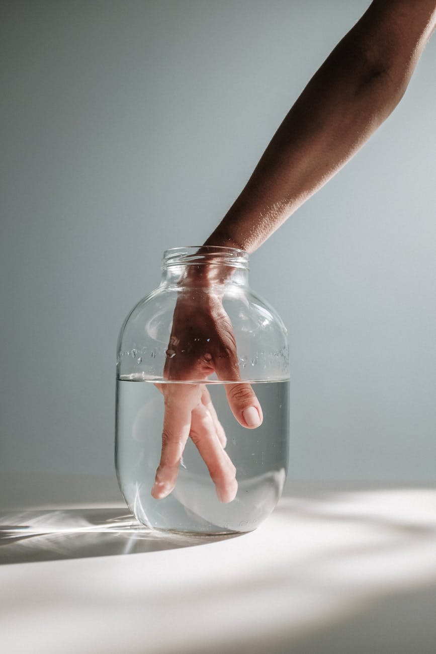 hand of a person inside a clear glass jar with water